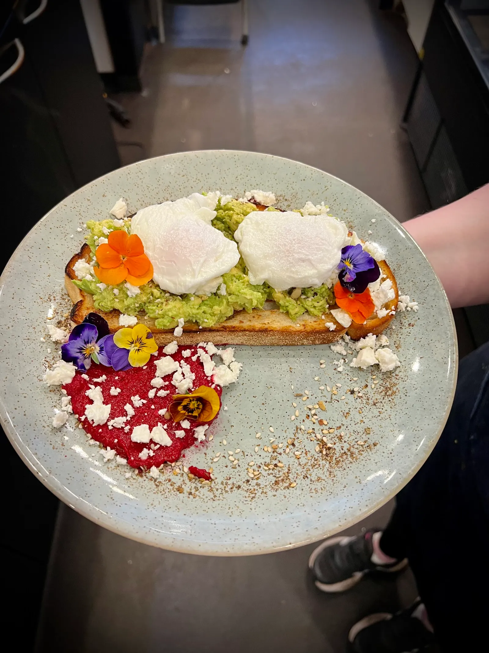Avocado toast with poached eggs, edible flowers and feta on a sage ceramic plate