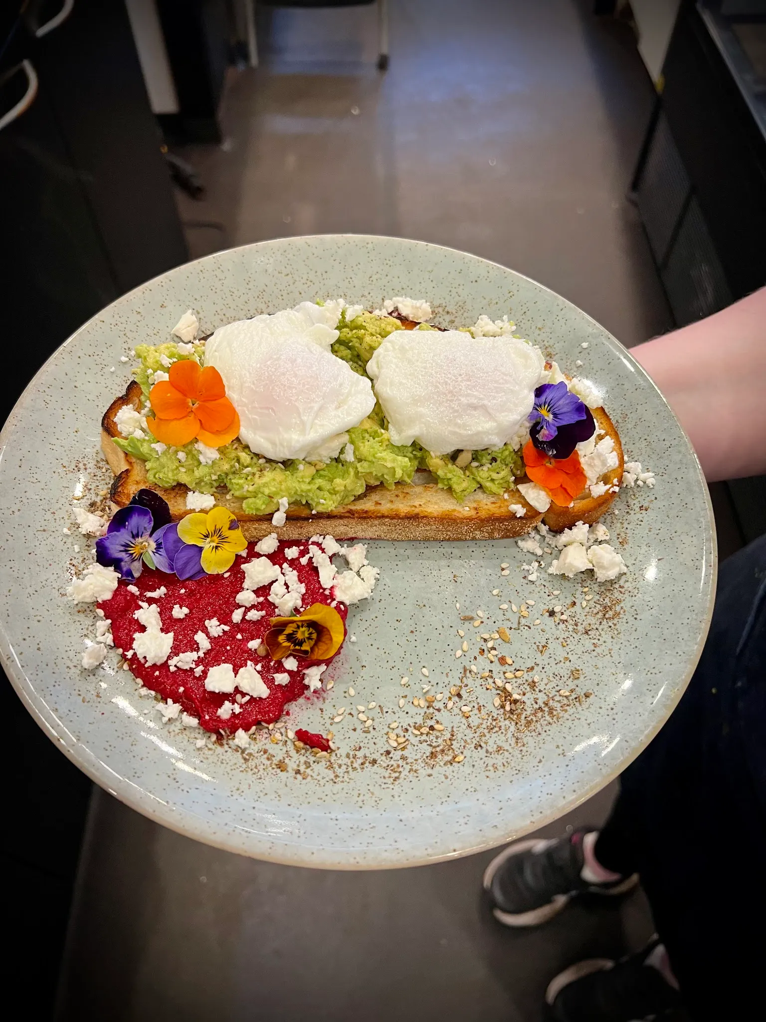 Avocado toast with poached eggs, edible flowers, feta, and salmon on a sage ceramic plate
