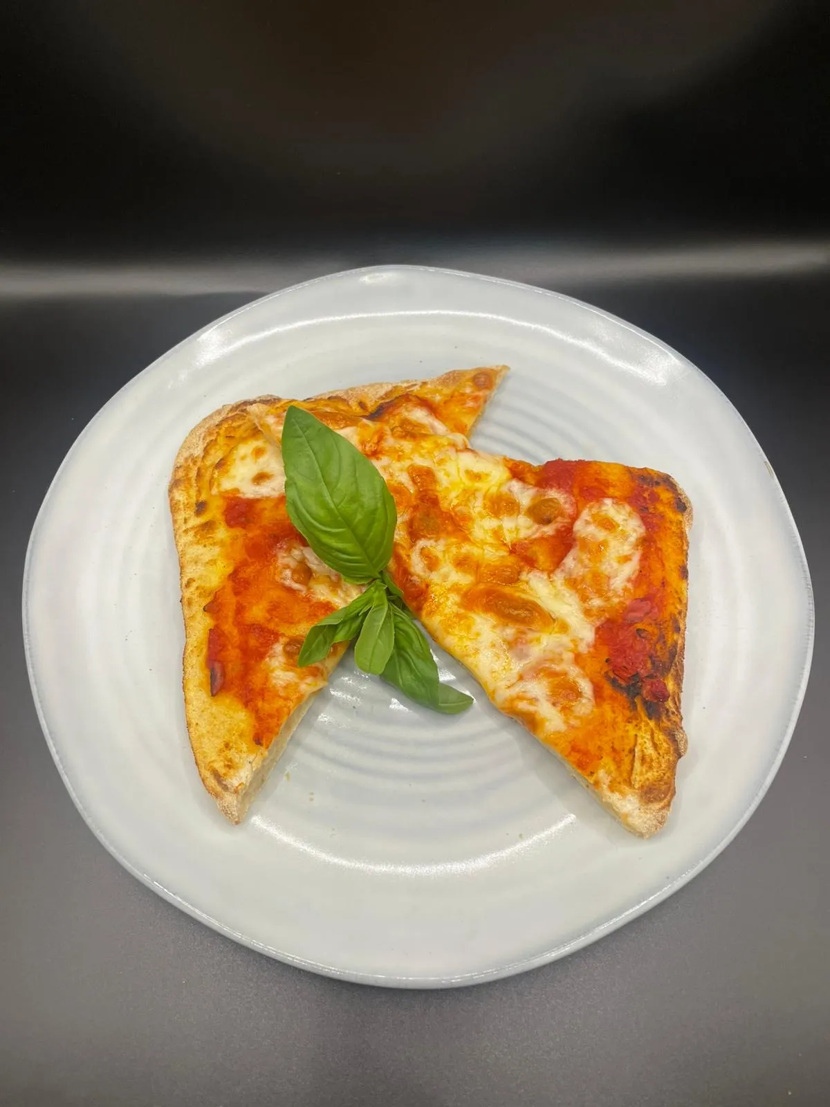 Margherita pizza slices with fresh basil on a white plate, dark background