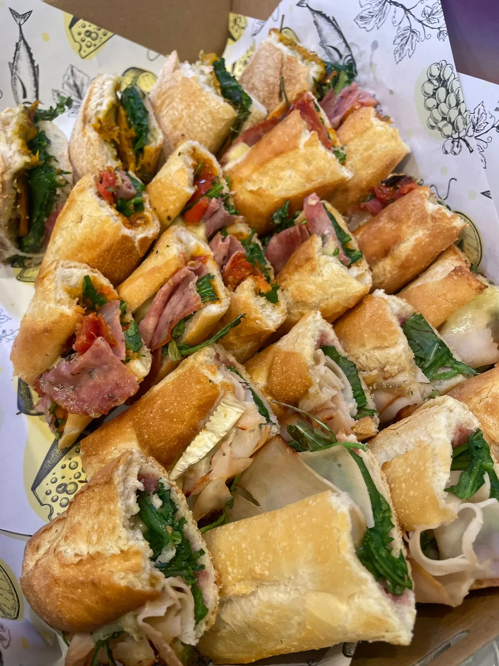 Catering platter of assorted gourmet sandwiches and rolls in a lined tray