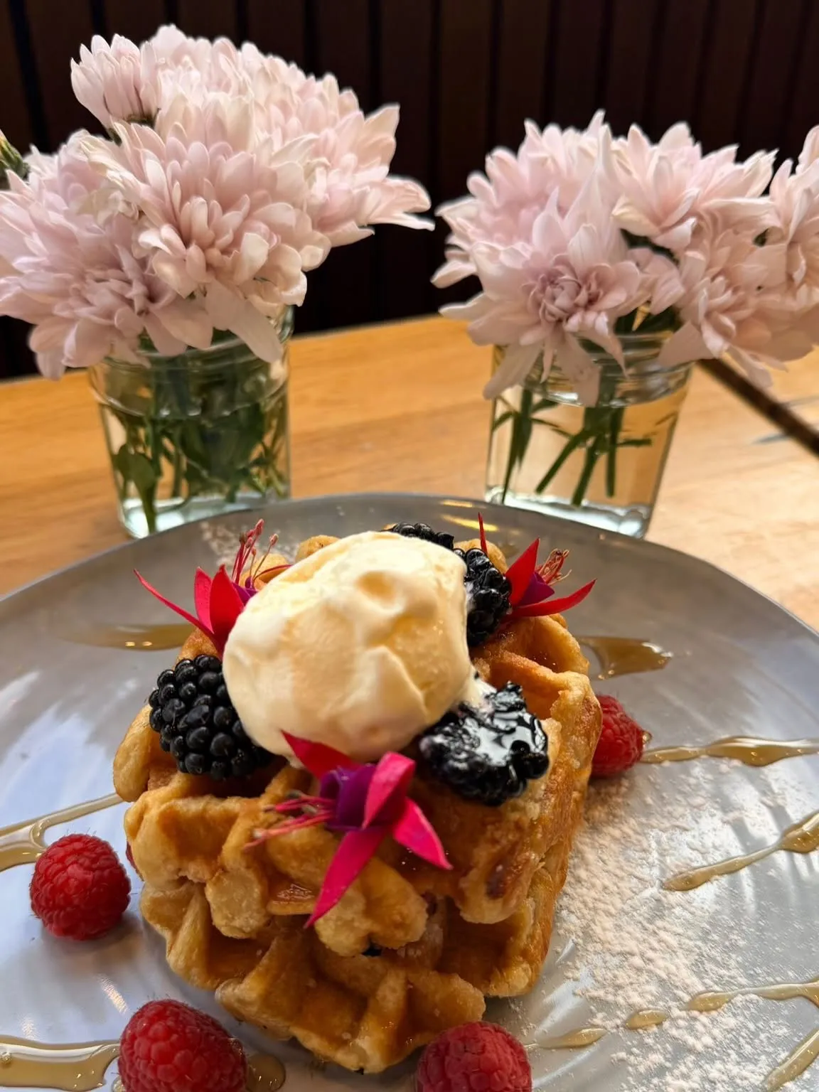 Golden waffle with ice cream, berries, edible flowers and syrup, pink chrysanthemums in background